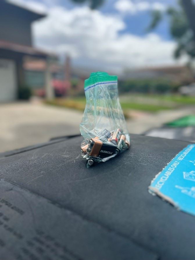Batteries in a plastic bag on top of a waste disposal cart.
